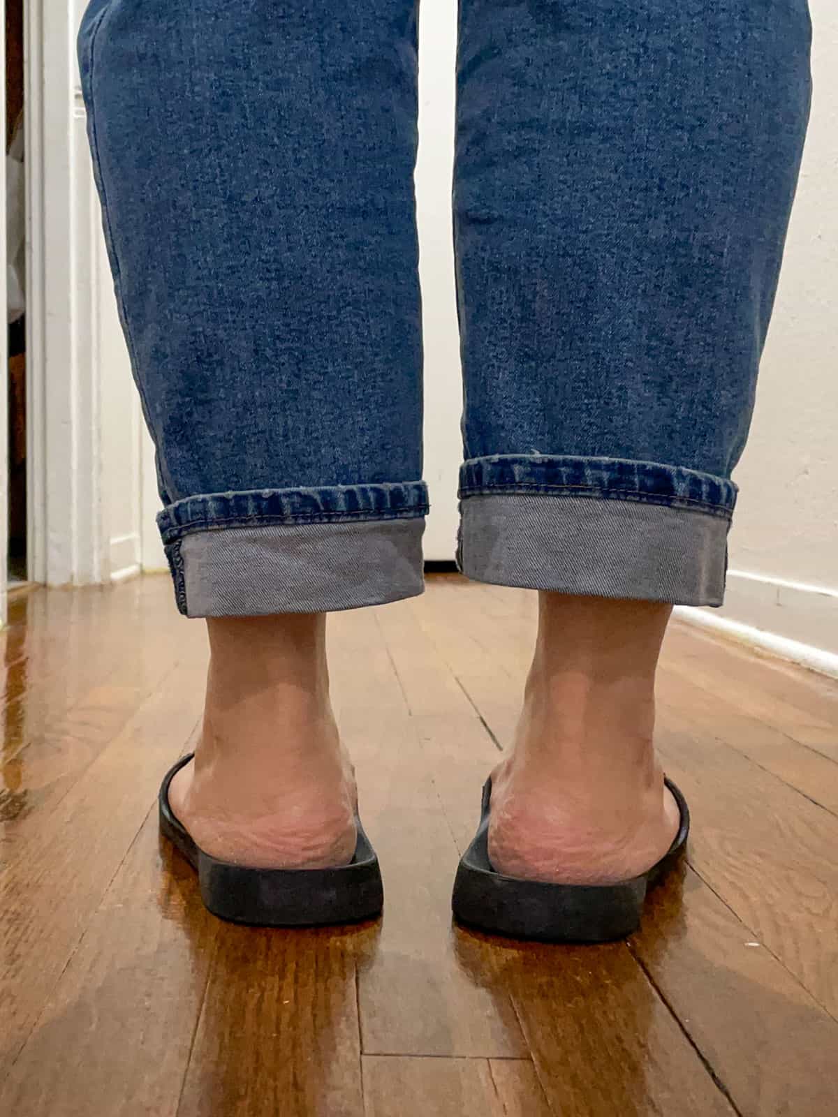 woman wearing jeans and Archie's black flip flops standing on a wooden floor inside