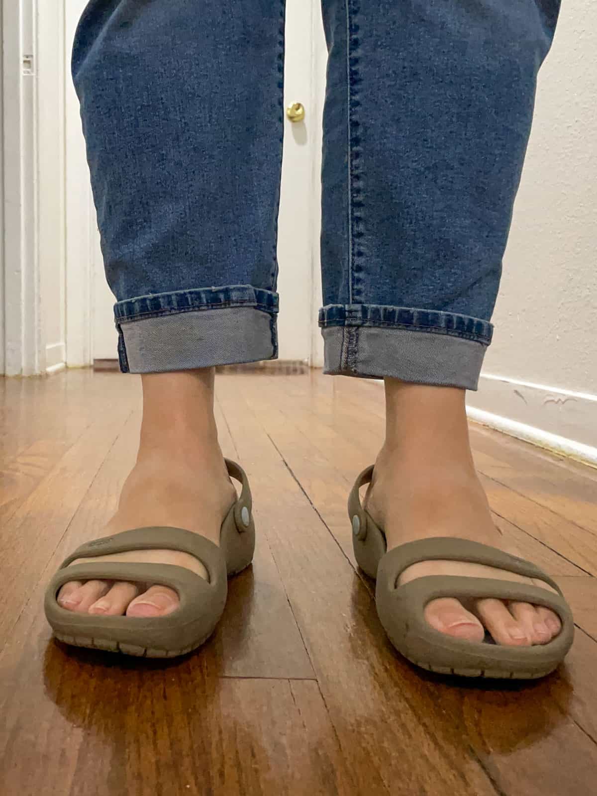 woman wearing jeans and Crocs sandals standing on a wooden floor inside